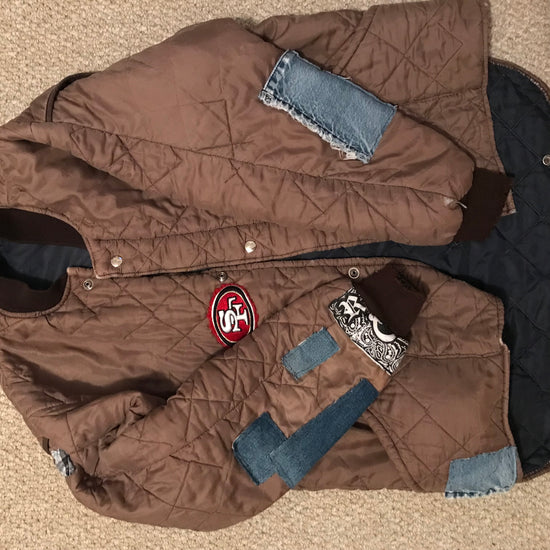 old brown jacket laid on floor patched up with small sewn in pieces of jean fabric